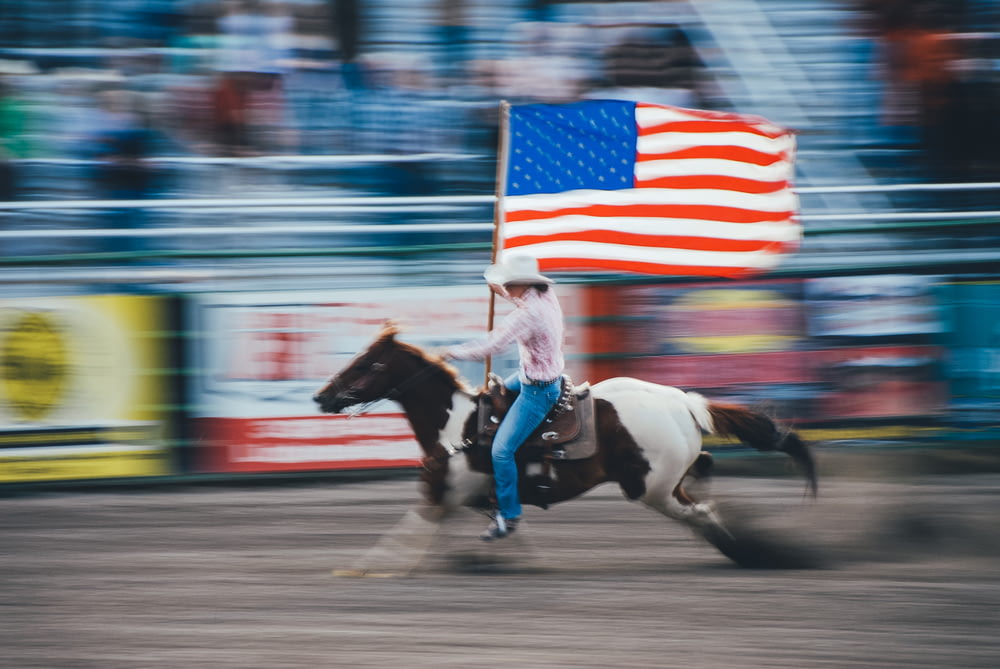 foto time lapse dell'uomo che porta la bandiera degli Stati Uniti mentre cavalca il cavallo marrone