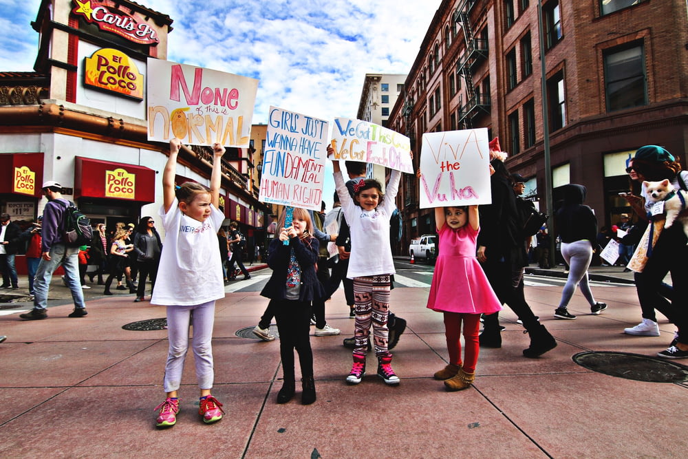 Quatre enfants brandissent une banderole au milieu d’une rue animée pendant la journée
