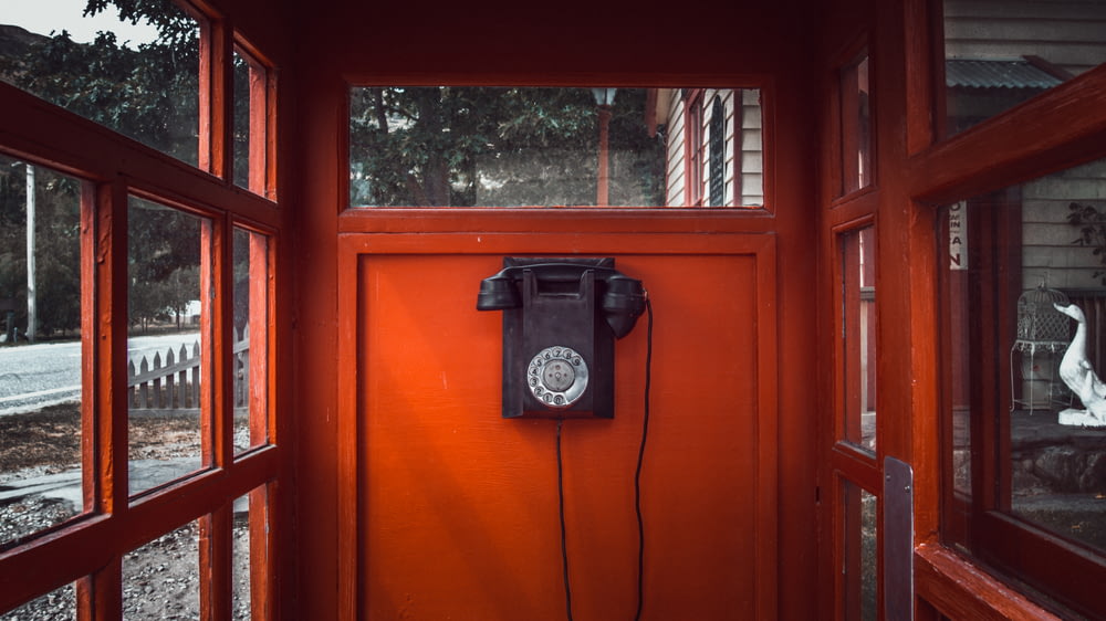 Teléfono de disco negro montado en una pared de madera roja