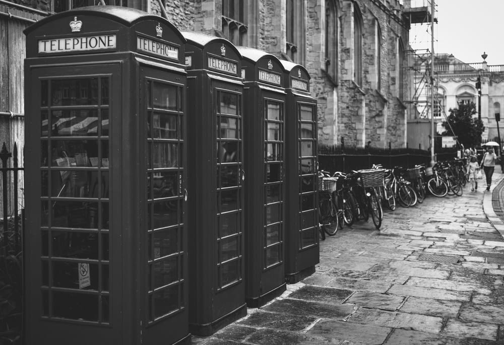 grayscale photo of four telephone booths lined up
