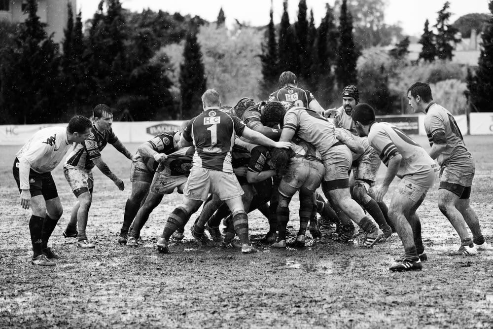 grayscale photography of men playing rugby on muddy land
