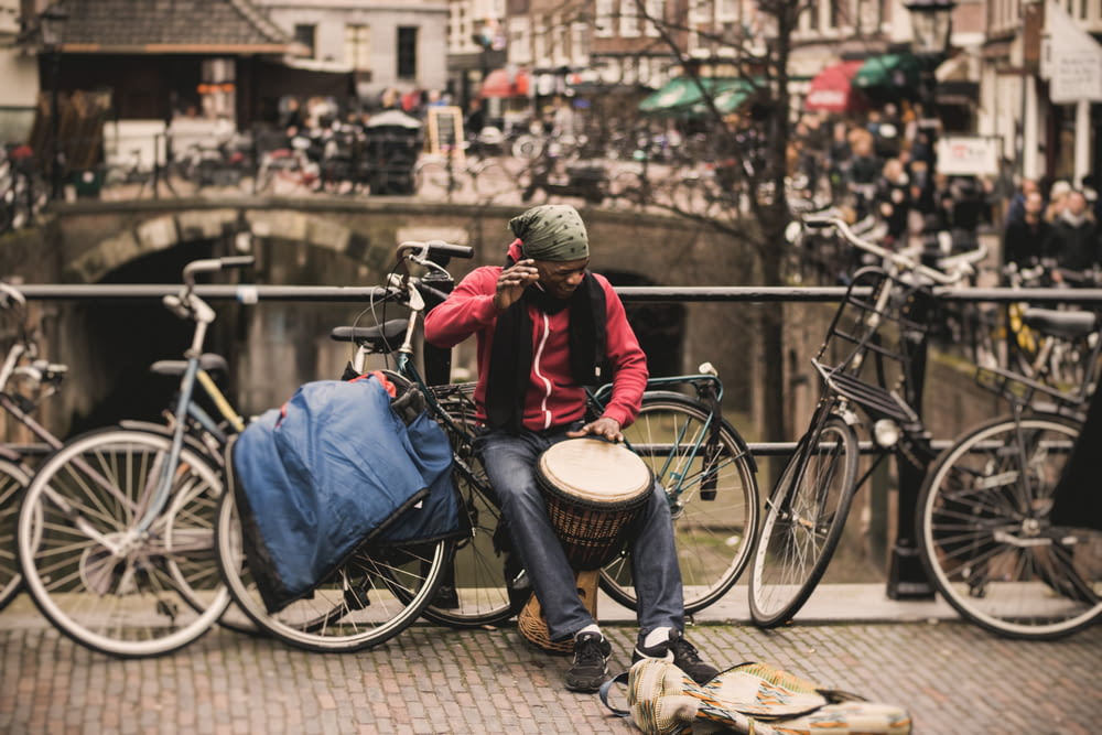 赤いシャツを着た男が、デッキレールの近くで灰色の自転車に座りながらダルブカドラムを演奏する