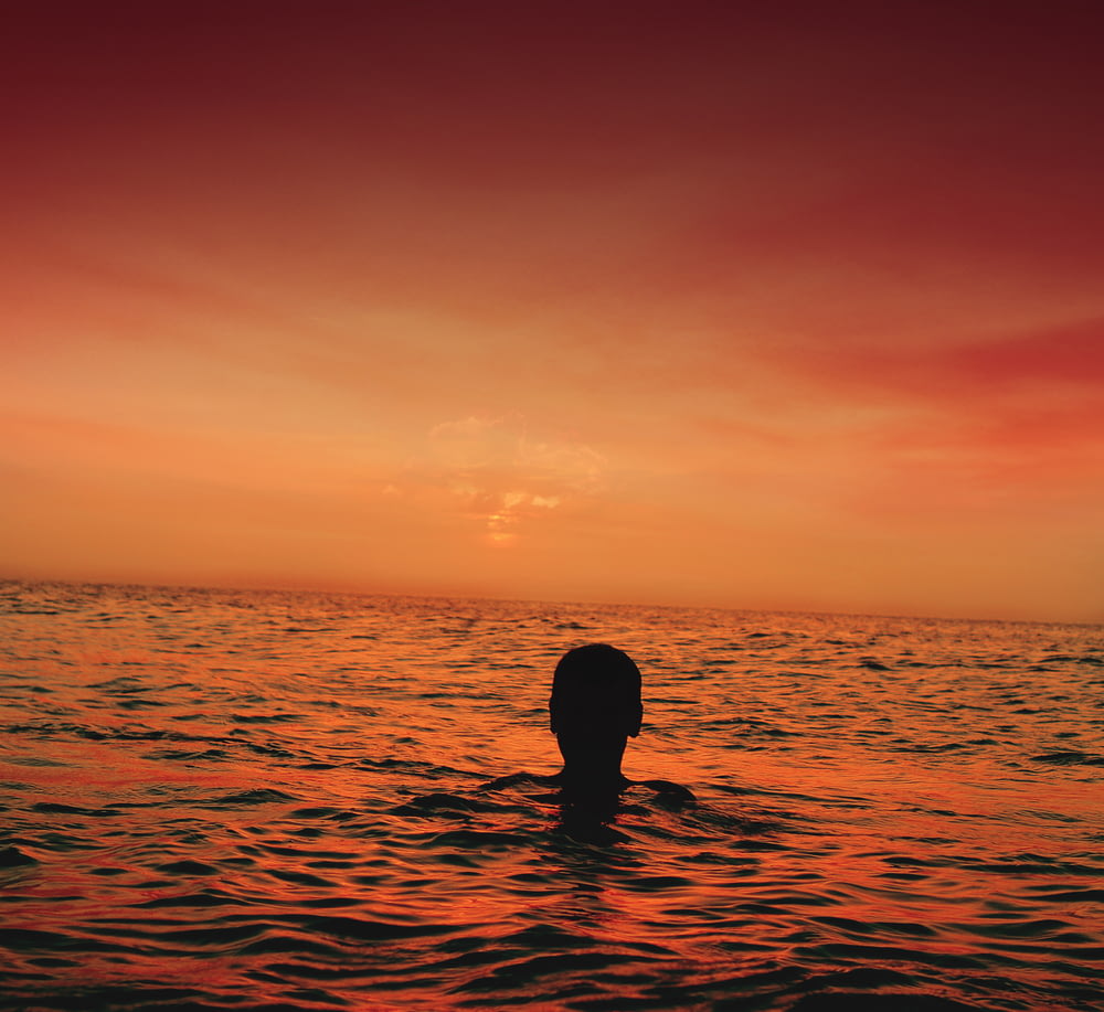 silhouette of person in ocean during sunset