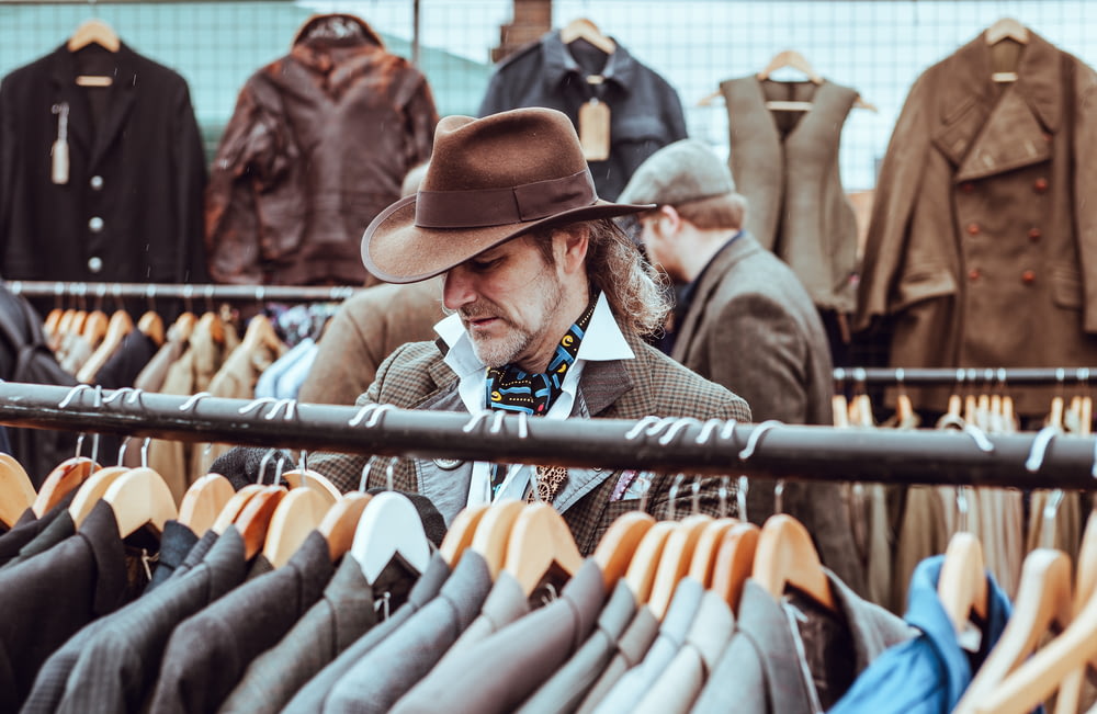 homem no chapéu de cowboy marrom na frente de jaquetas de terno penduradas