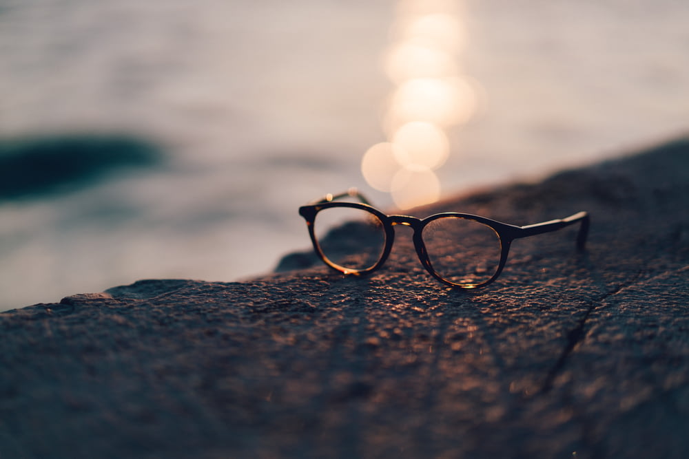 Nahaufnahme einer schwarz gerahmten Sonnenbrille mit klarem Glas in der Nähe eines Gewässers