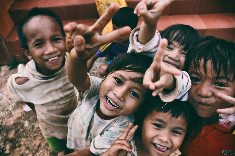 cinq enfants souriant tout en faisant le signe de la main de la paix