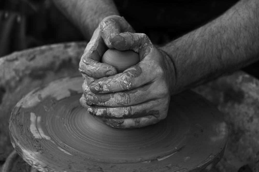 grayscale photography of person's hand making pot