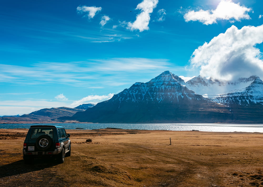 Stationnement SUV sur un terrain brun face au lac à travers la montagne noire enneigée pendant la journée