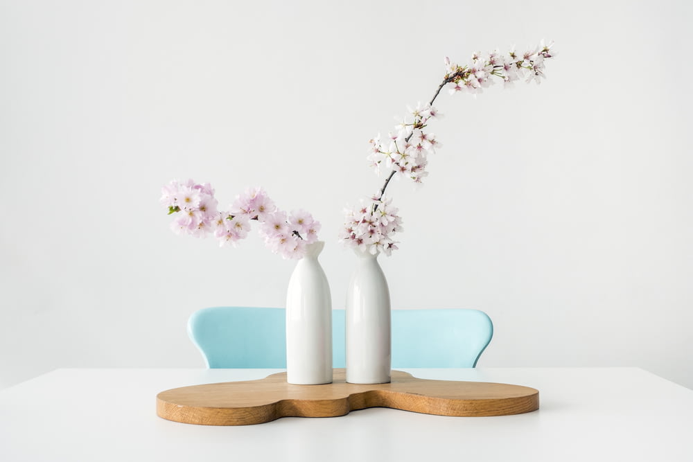 two pink petaled flowers in white vases on brown wooden surface