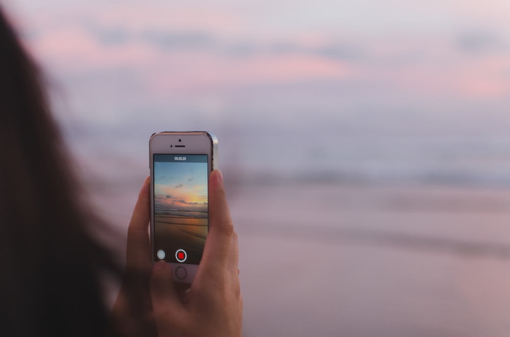 persona que toma una foto del mar abierto y la puesta del sol