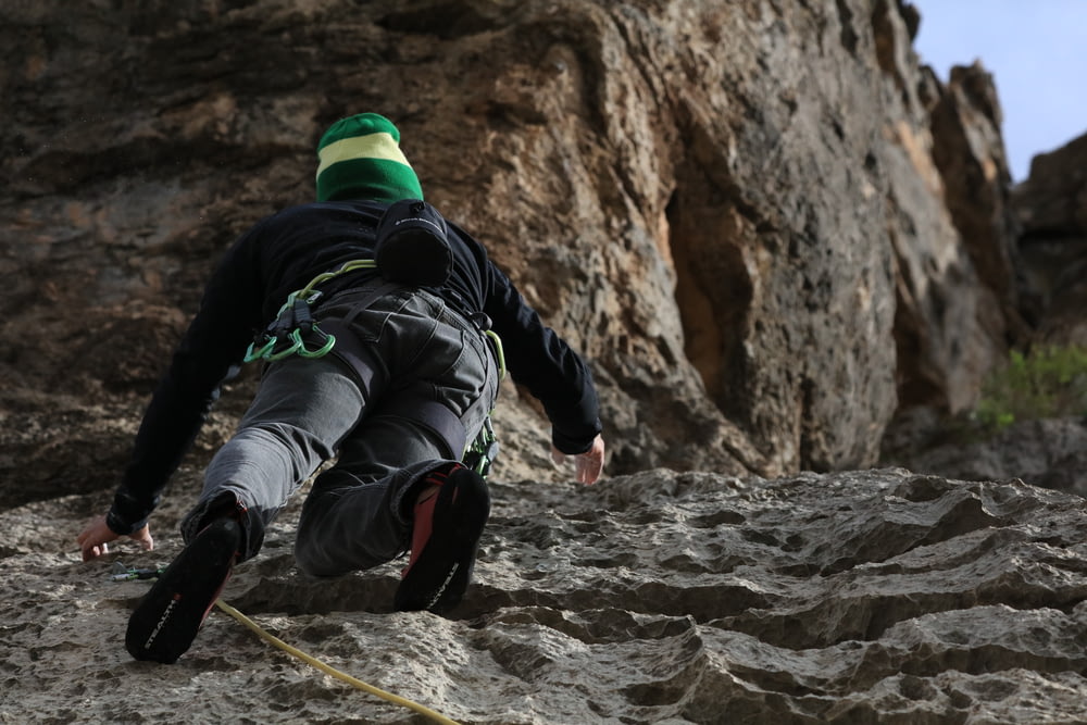 man in black jacket and green pants climbing on brown rocky mountain during daytime