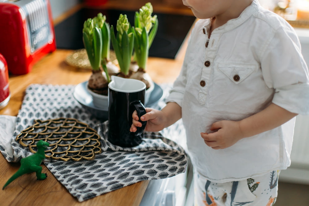 criança segurando caneca de cerâmica preta e branca enquanto está perto da mesa