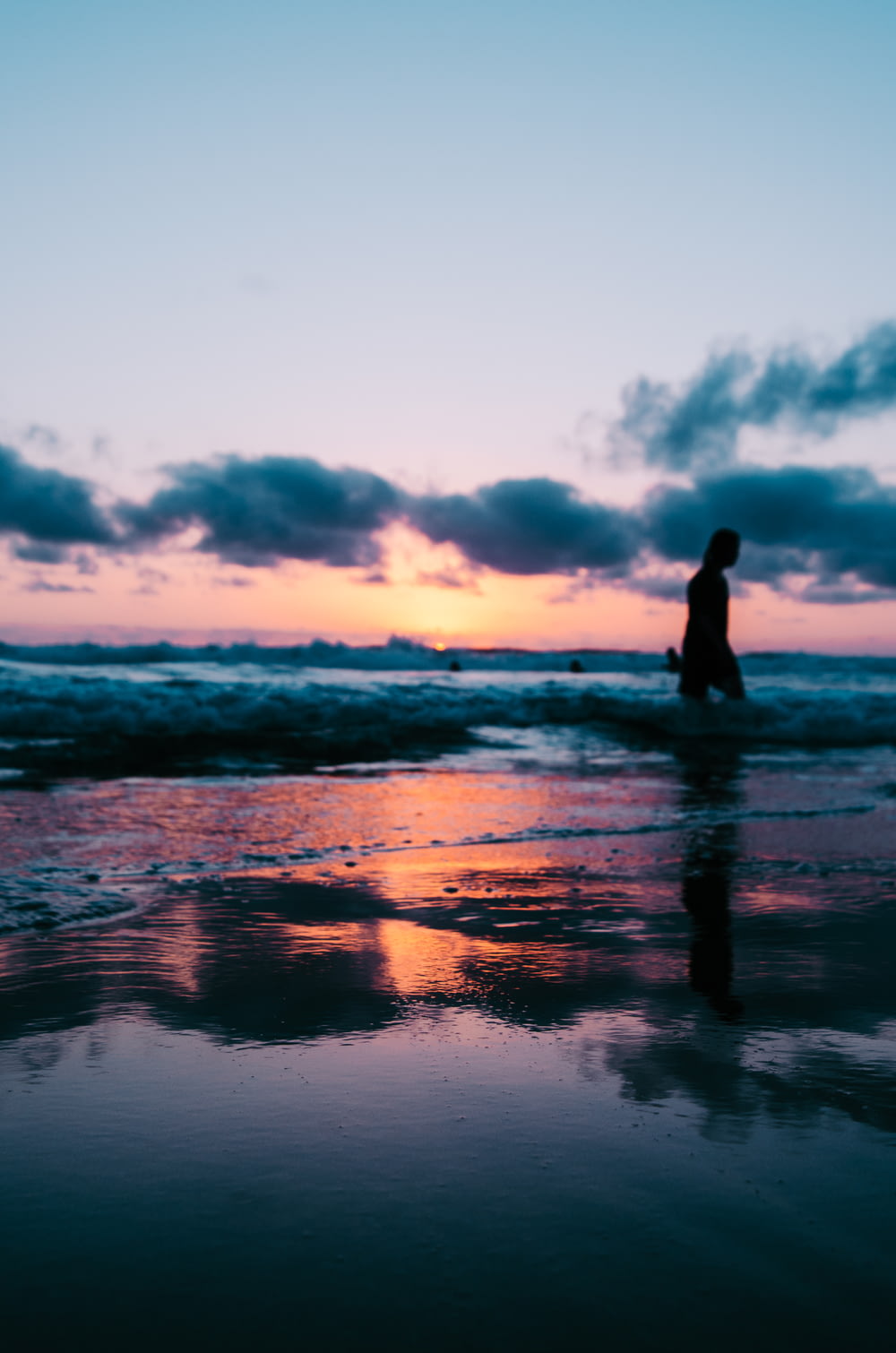 silhouette photo of a person walking on seashore under cloudy sky during golden hour