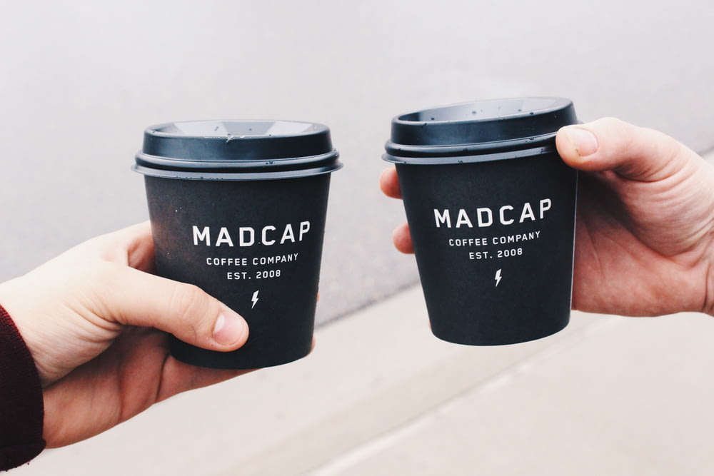 two person holding black Madcap coffee disposable cups
