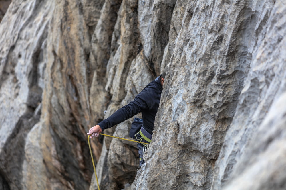 man in black jacket climbing on gray rock mountain during daytime