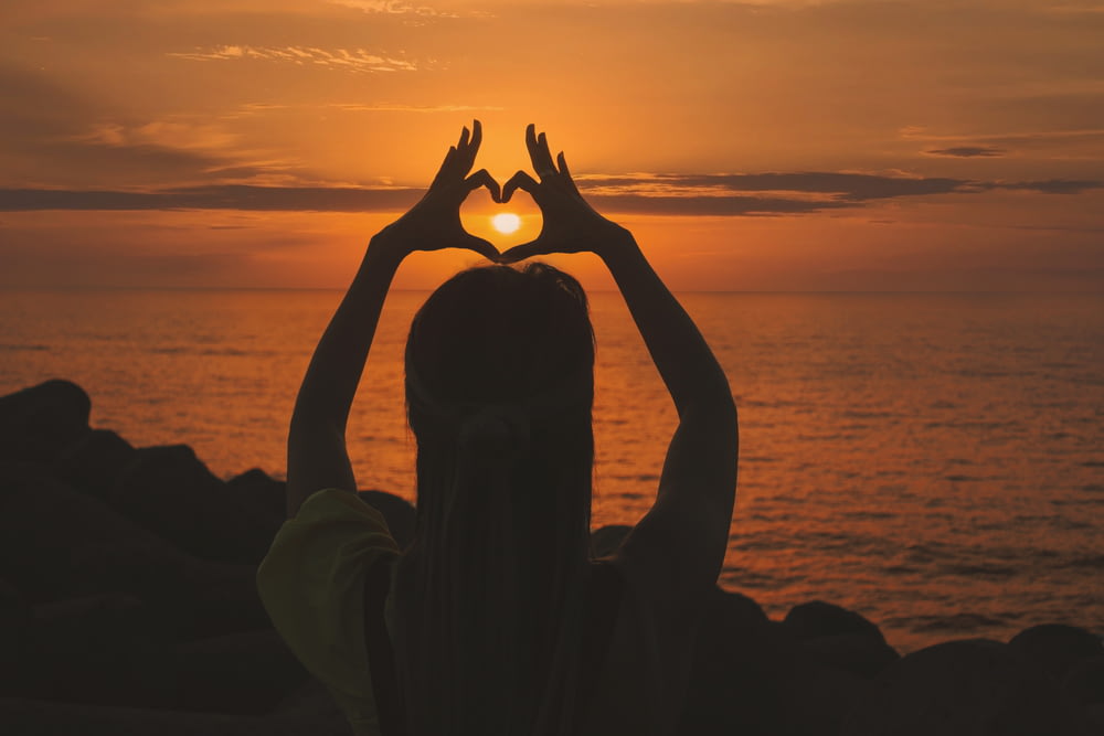 silhueta da mulher fazendo sinal do coração durante o pôr do sol