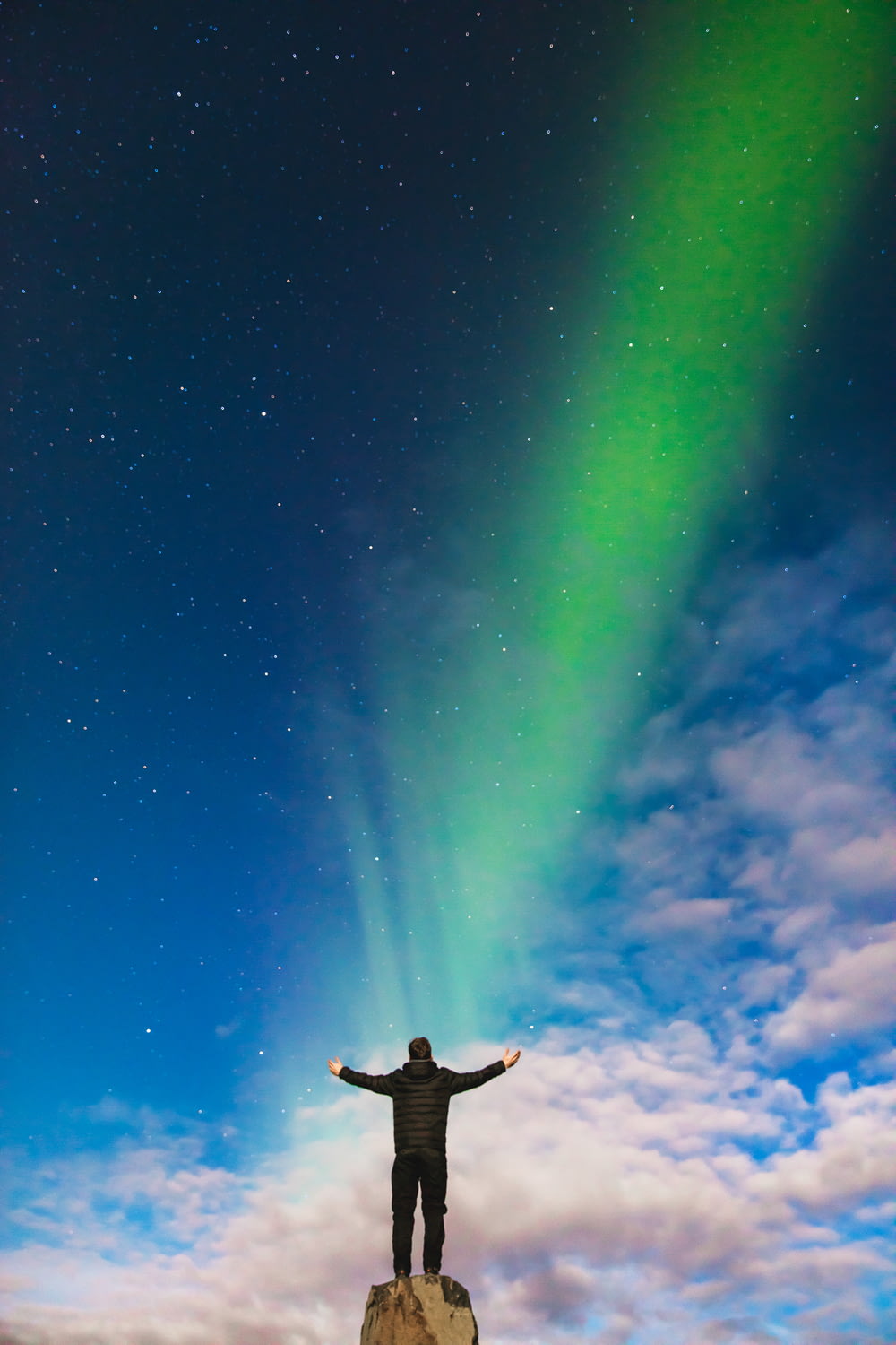 Uomo in piedi sulla roccia sotto l'aurora boreale verde e le nuvole bianche