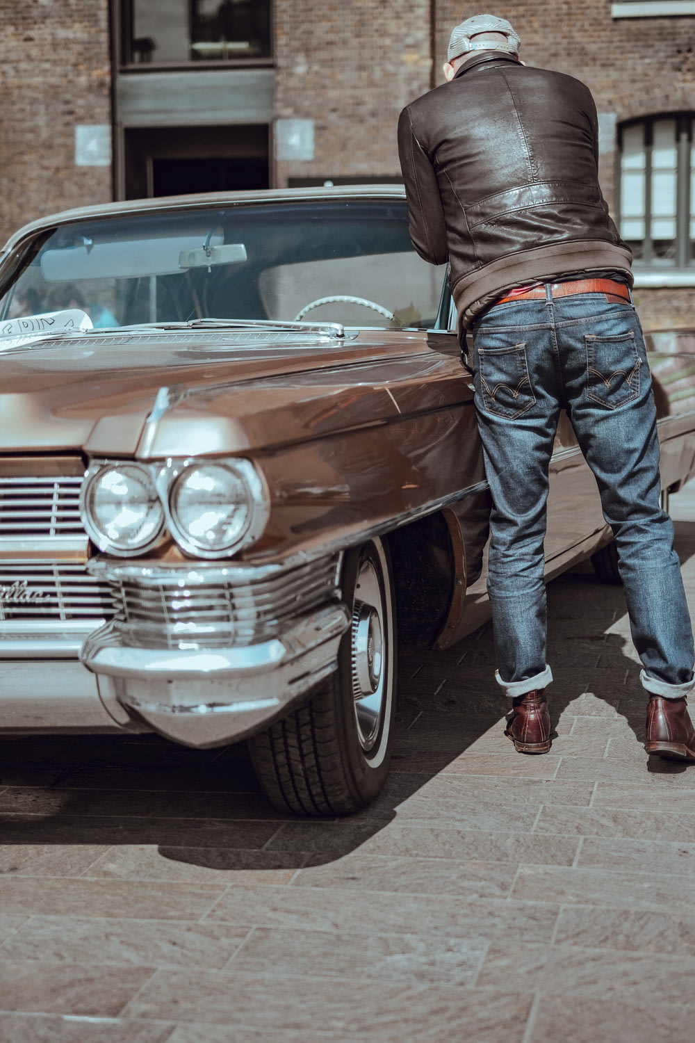 Mann in blauer Jeanshose steht neben braunem Auto