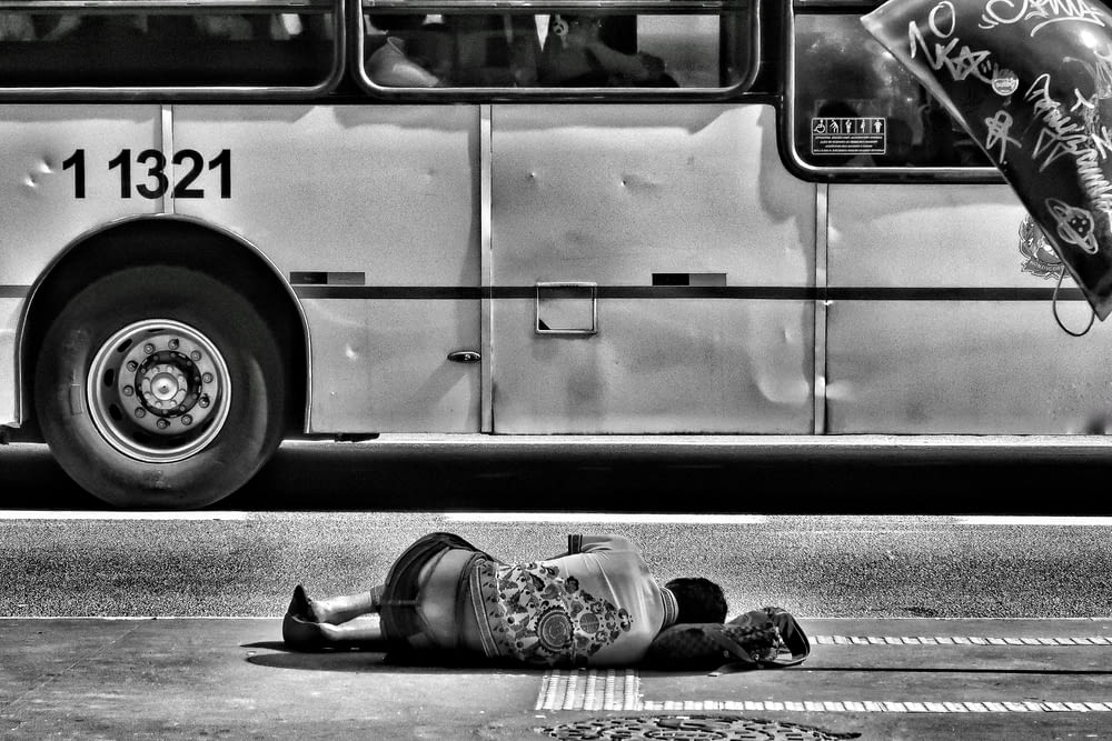 grayscale photography of person laying on ground near bus