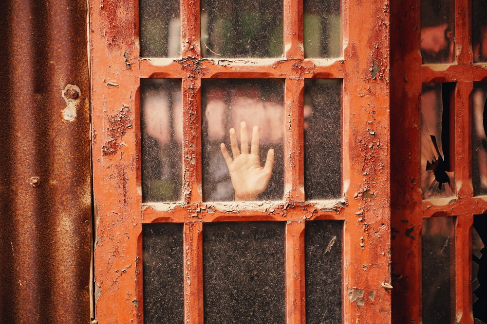 person hand on glass panel door with red wooden frame