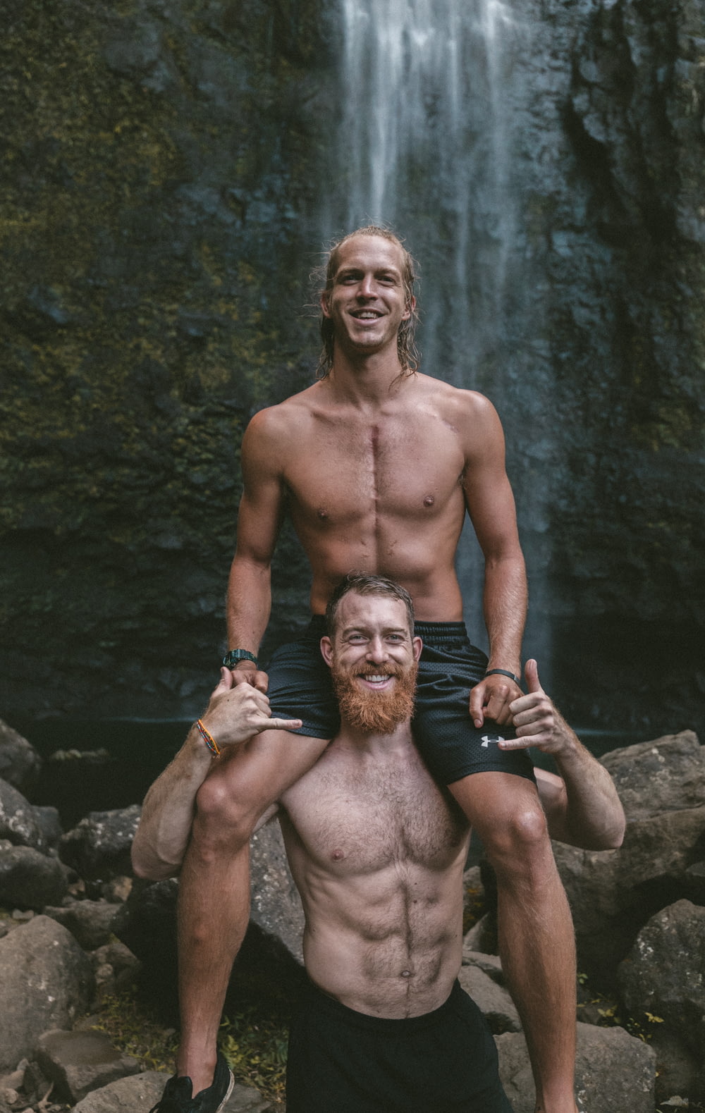 a man is holding a man on his shoulders in front of a waterfall