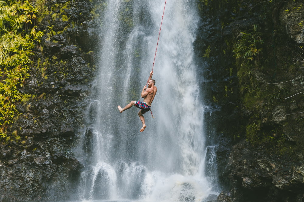 man hanging on rope near waterfalls during daytime