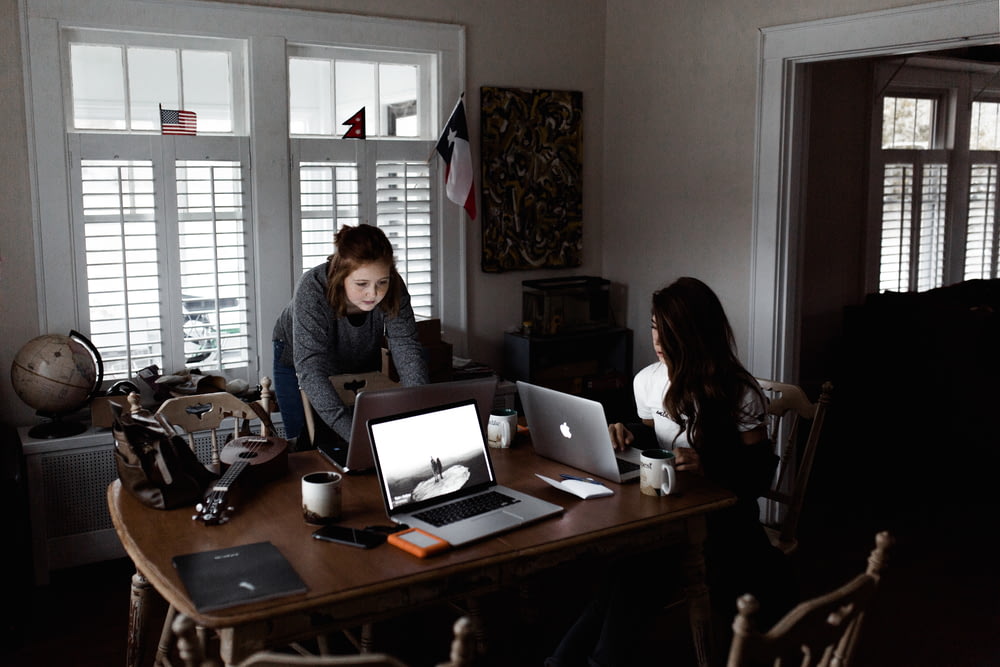 donne che usano il computer portatile sul tavolo di legno marrone