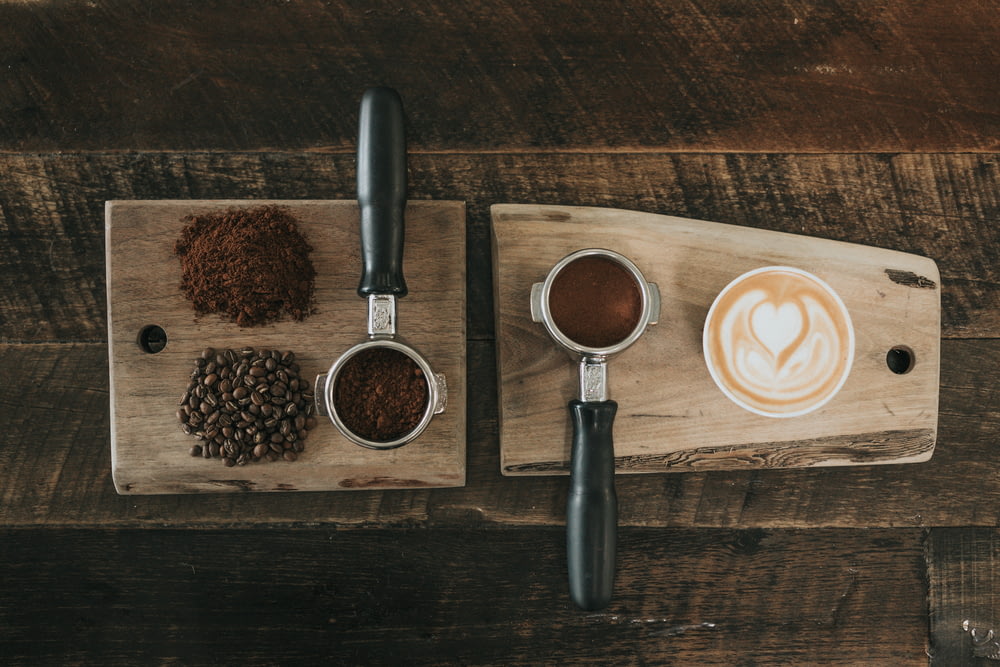 grãos de café ao lado do pó de café na placa de madeira marrom