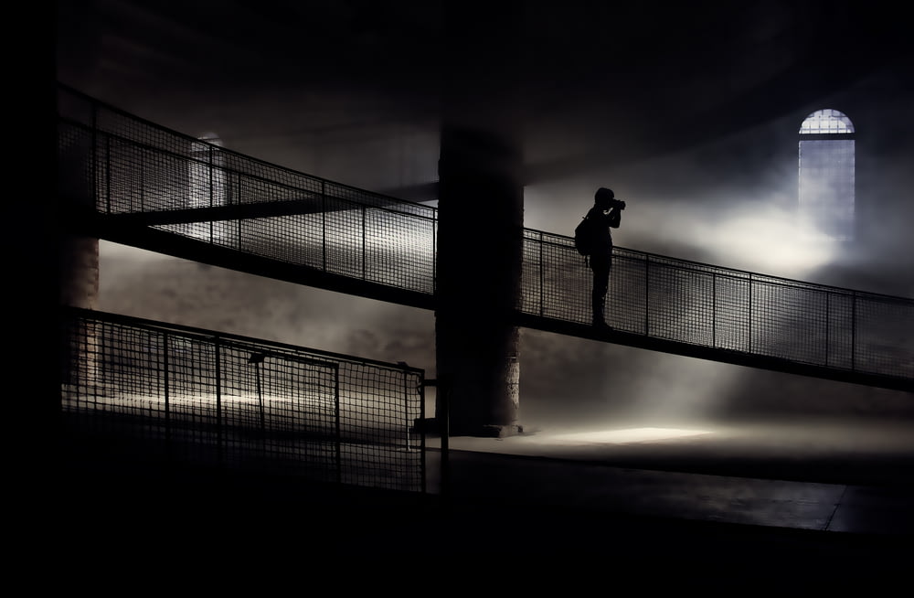 silhouette of person standing on bridge while taking photo