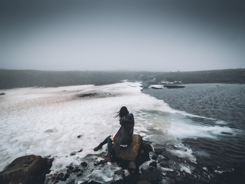 woman sitting on rock near seashore