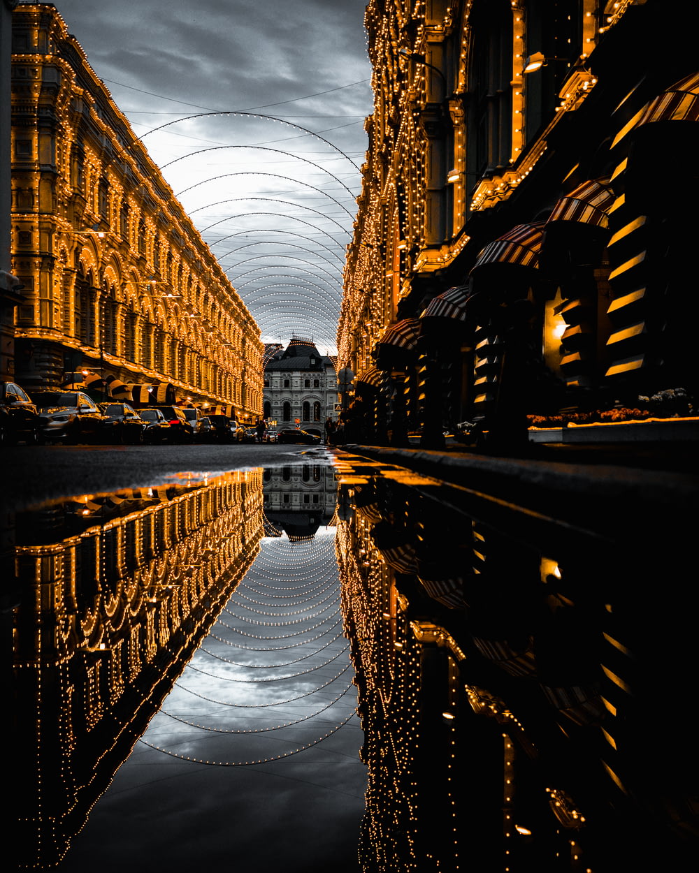 water on asphalt road with reflection of fully-decorated buildings under cloudy sky
