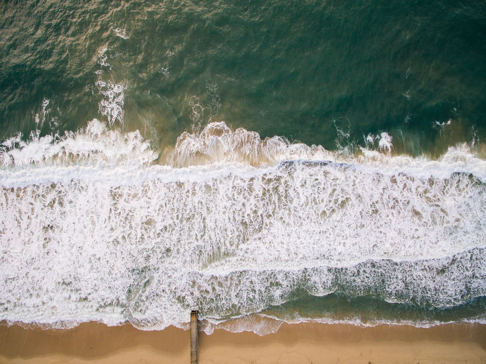 Draufsicht auf braunen Strandsand mit blaugrünem Meerwasser während des Tages