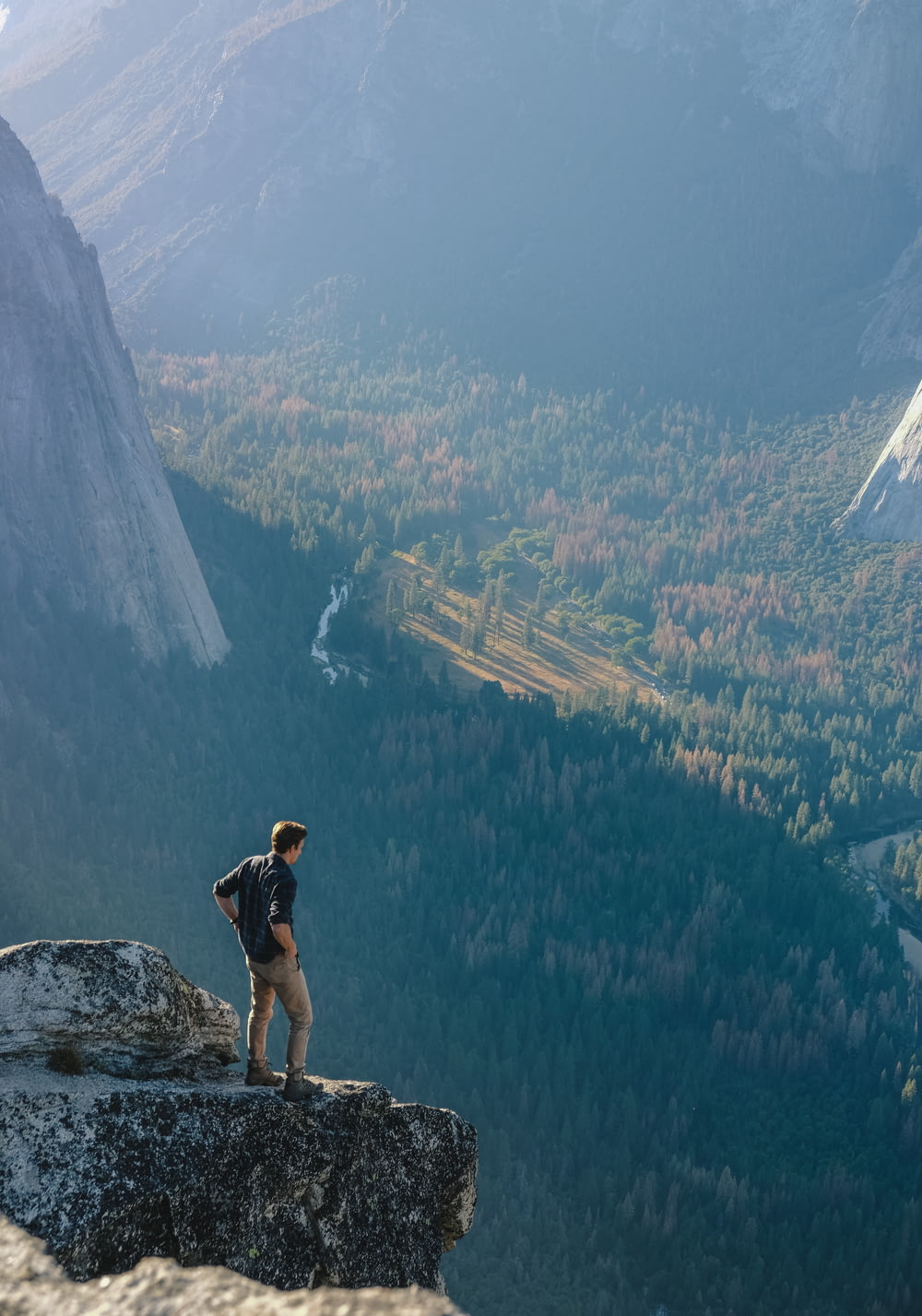Hombre de pie en la roca gris en el acantilado con la visión general del bosque durante el día