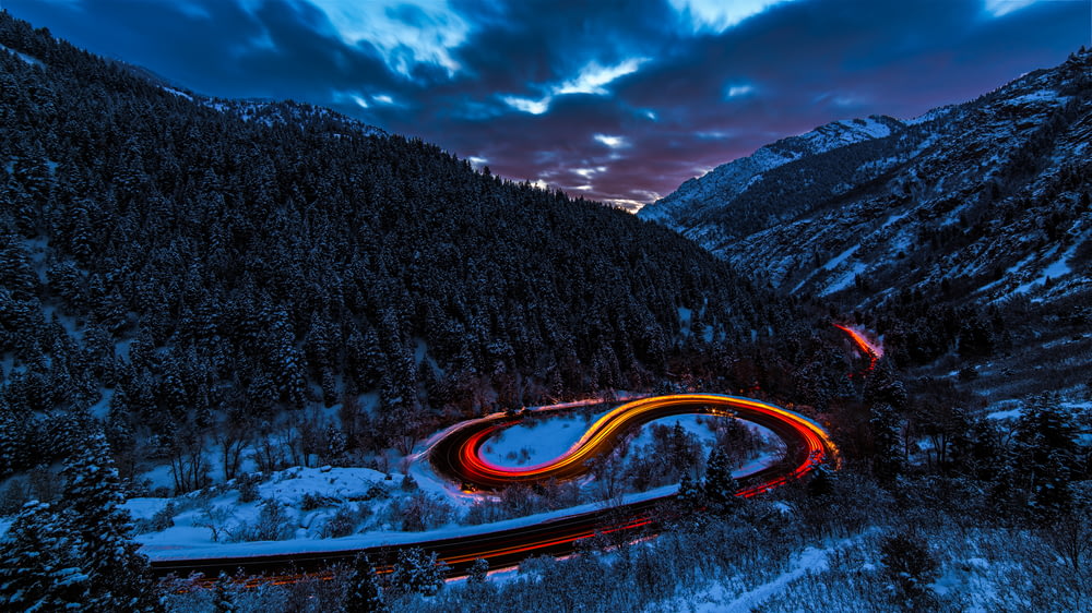 timelapse photography of curved road between mountain with trees