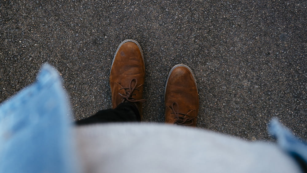 person wearing pair of brown leather boots standing on asphalt surface