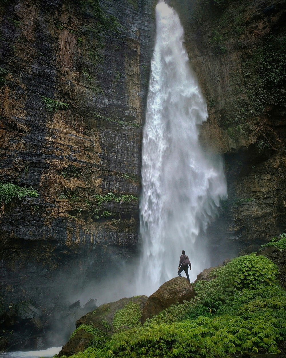 Person, die tagsüber auf einer braunen Felsformation steht und Wasserfälle betrachtet