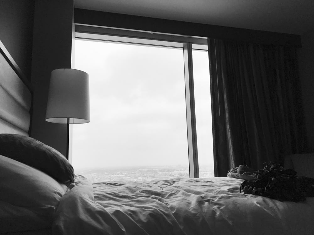 Foto en escala de grises de la cama cerca de una lámpara de mesa blanca