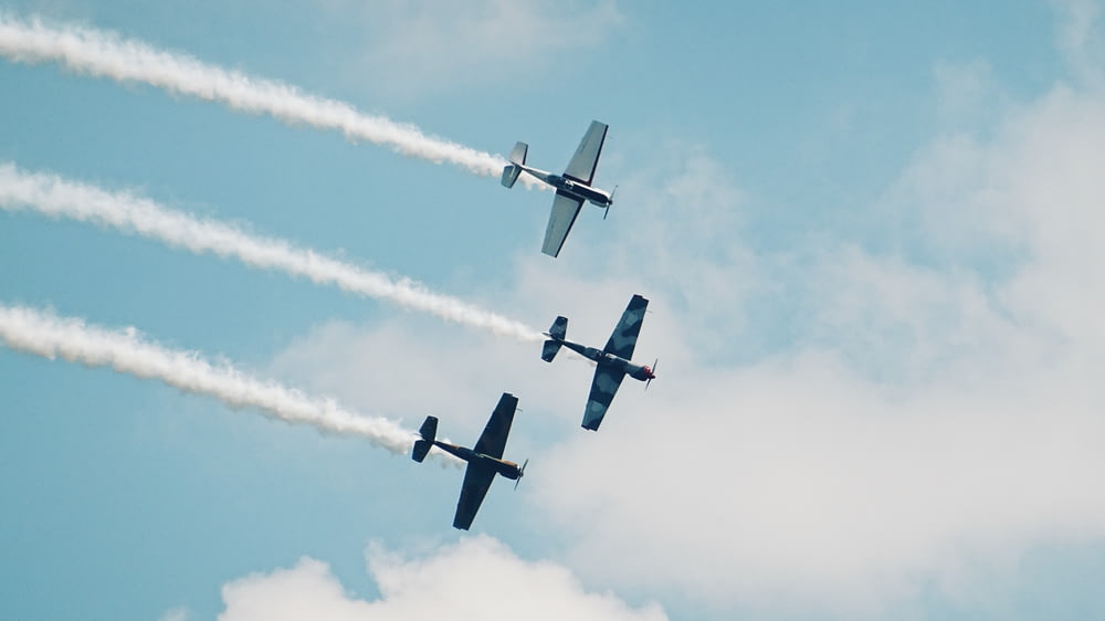 black, blue, and gray monoplanes in mid-air under white clouds