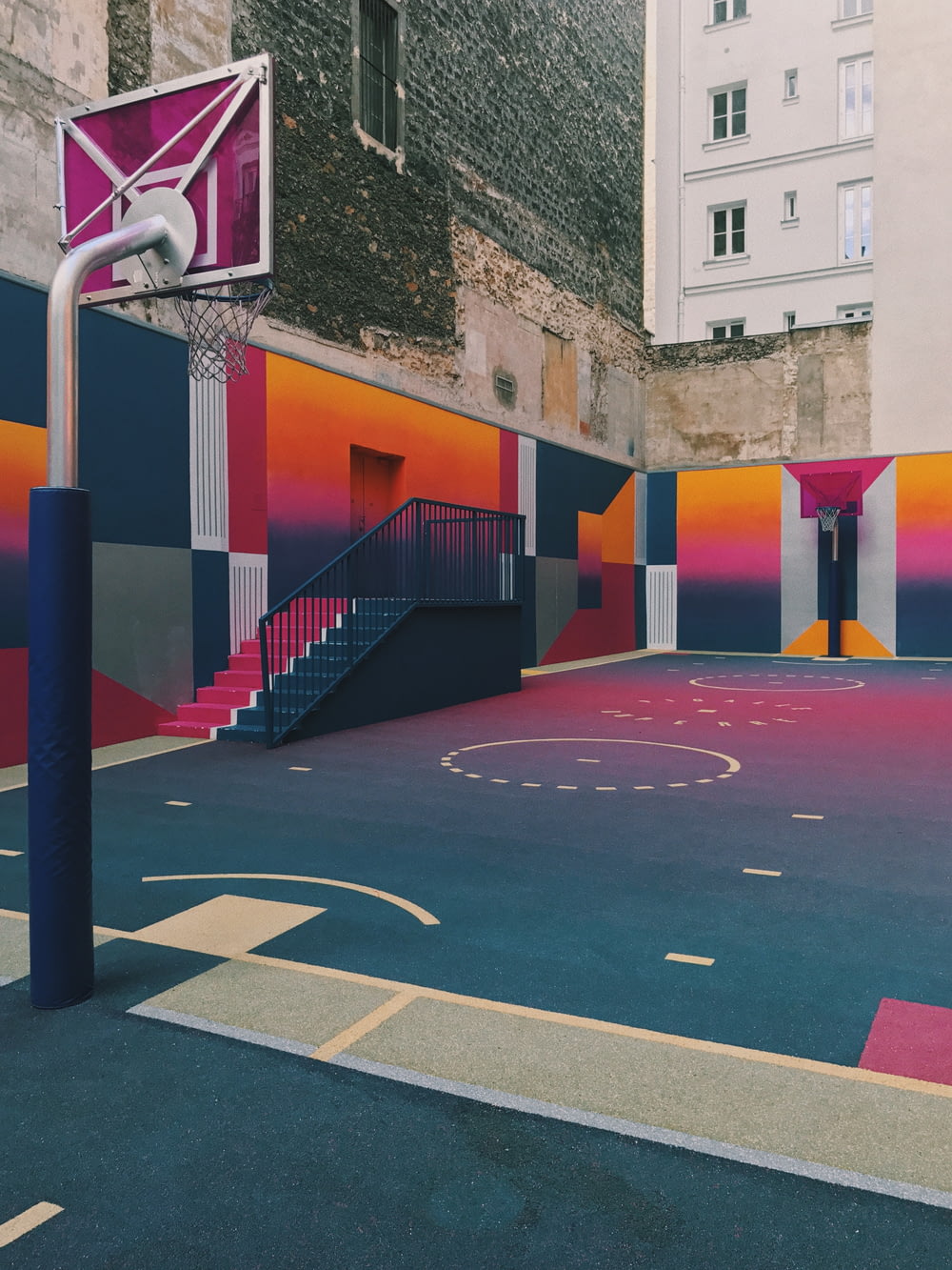 campo da basket nero, viola e arancione accanto a edifici in cemento durante il giorno