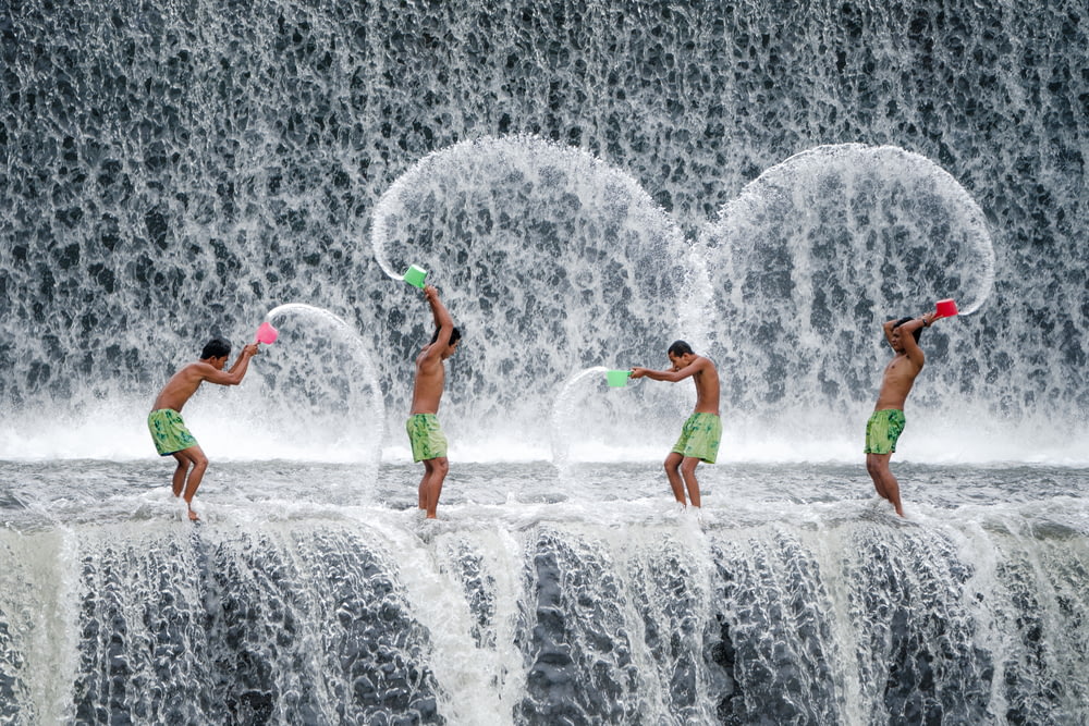 four men throwing dipper of water on waterfalls during daytime