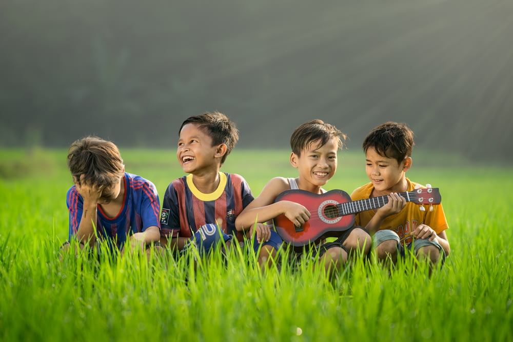 Cuatro niños riendo y sentados en la hierba durante el día