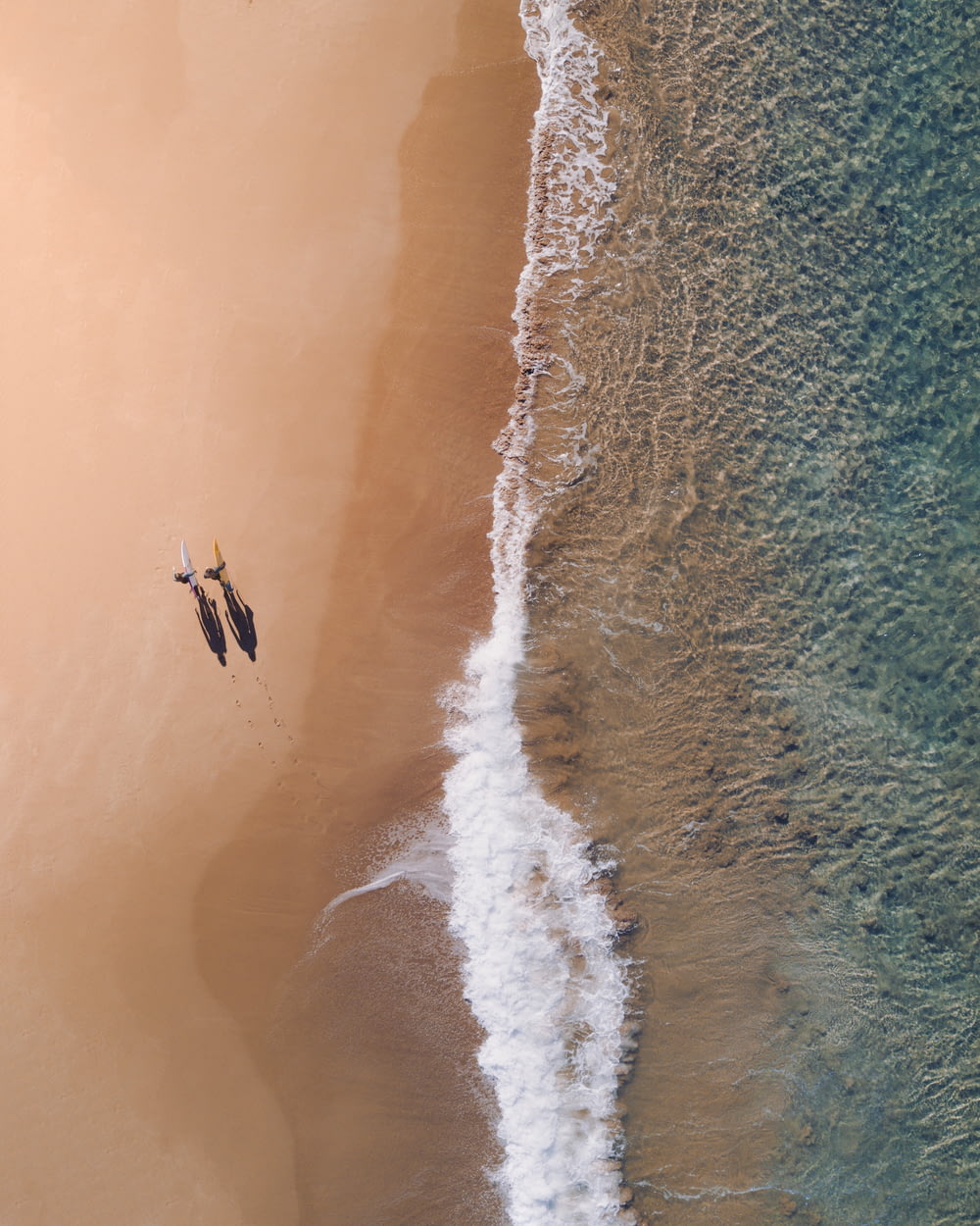 Luftaufnahme von zwei Personen, die tagsüber am Meer entlang spazieren