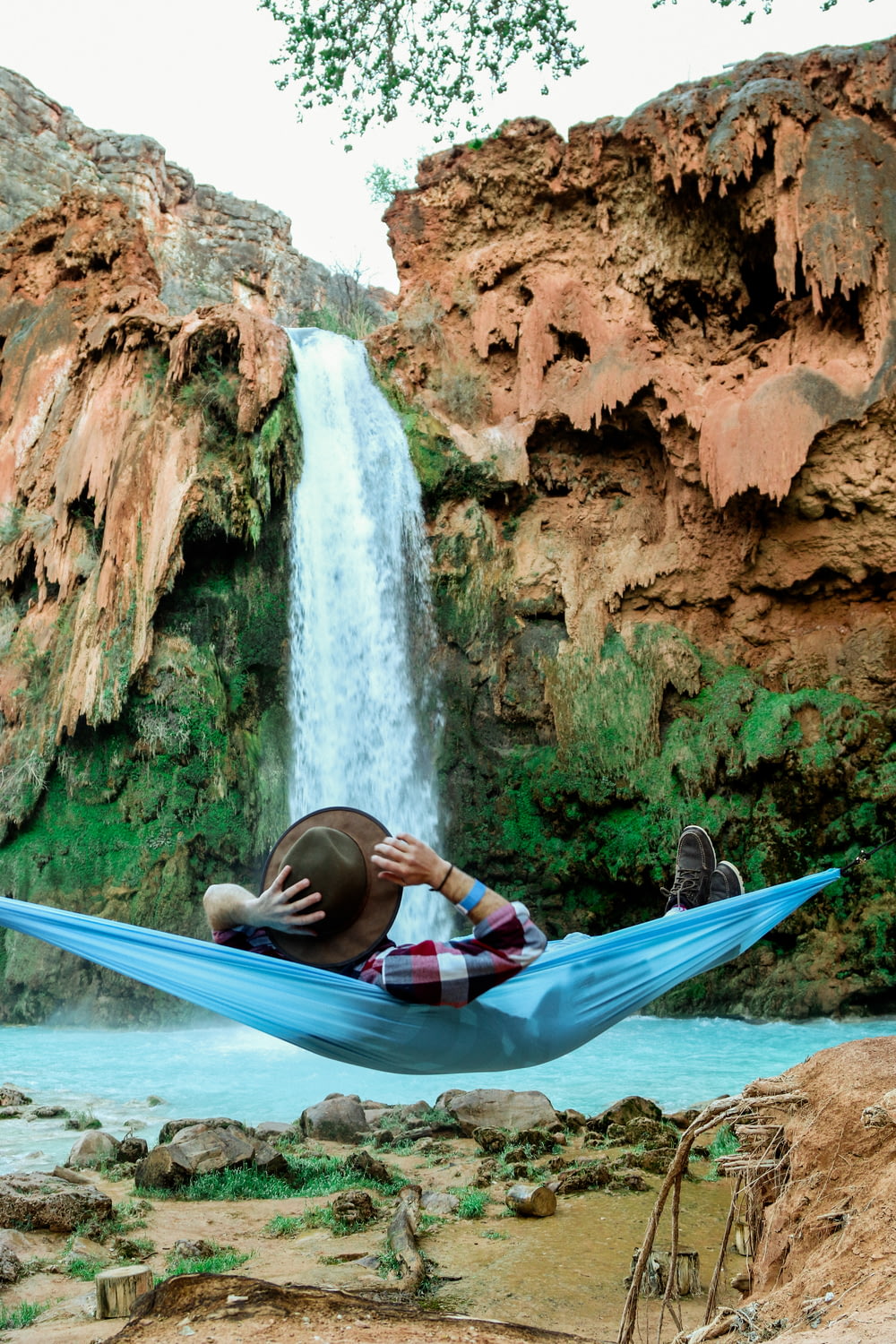 滝の前で青いハンモックに横たわる男