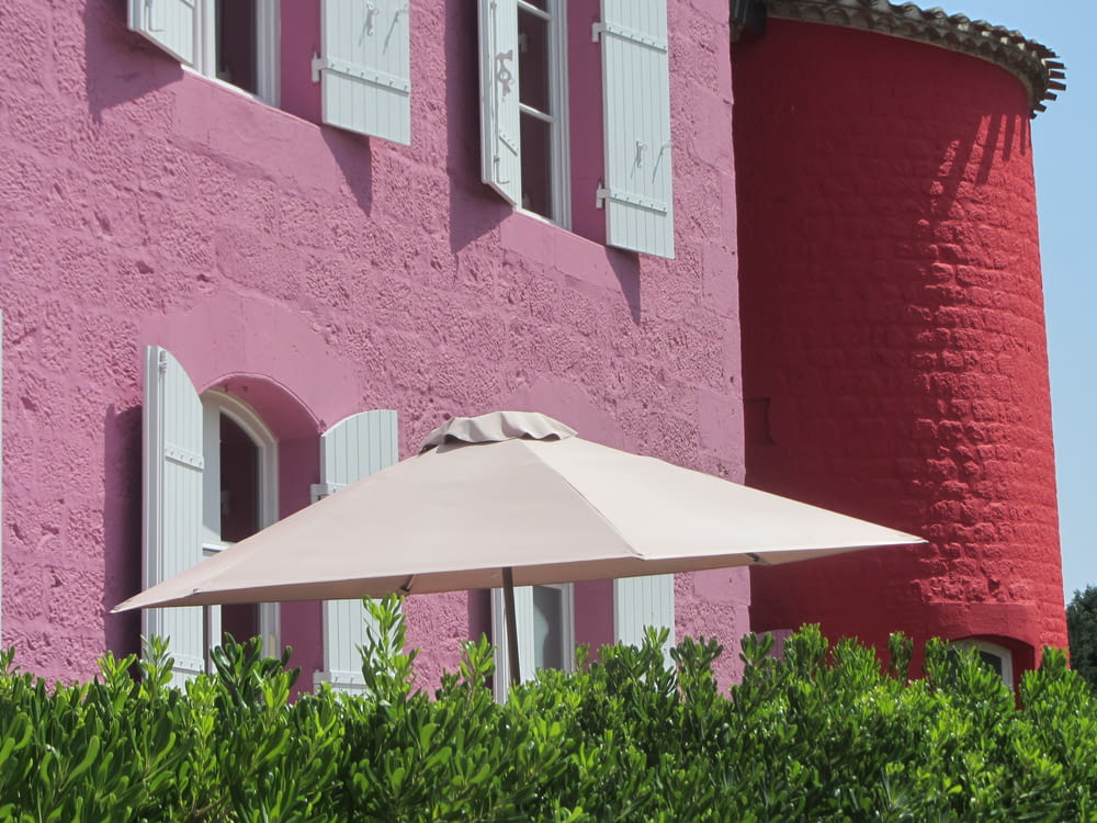 sombrilla de patio detrás de las plantas cerca de un edificio de hormigón pintado de rosa