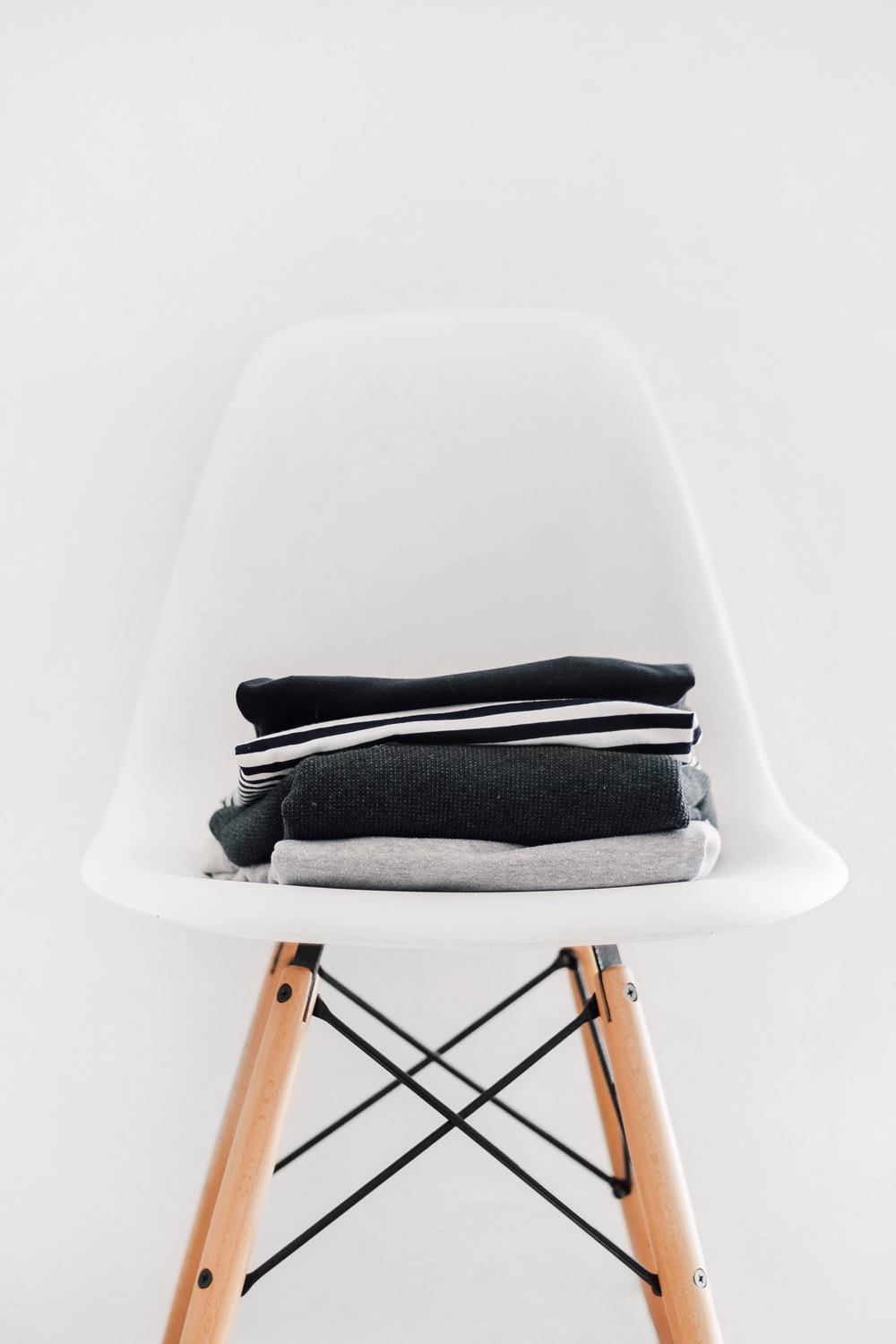 pila de textiles negros, blancos y grises en una silla acolchada blanca con marco marrón