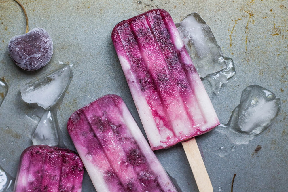 purple and white ice pop lying on wet ground with ice