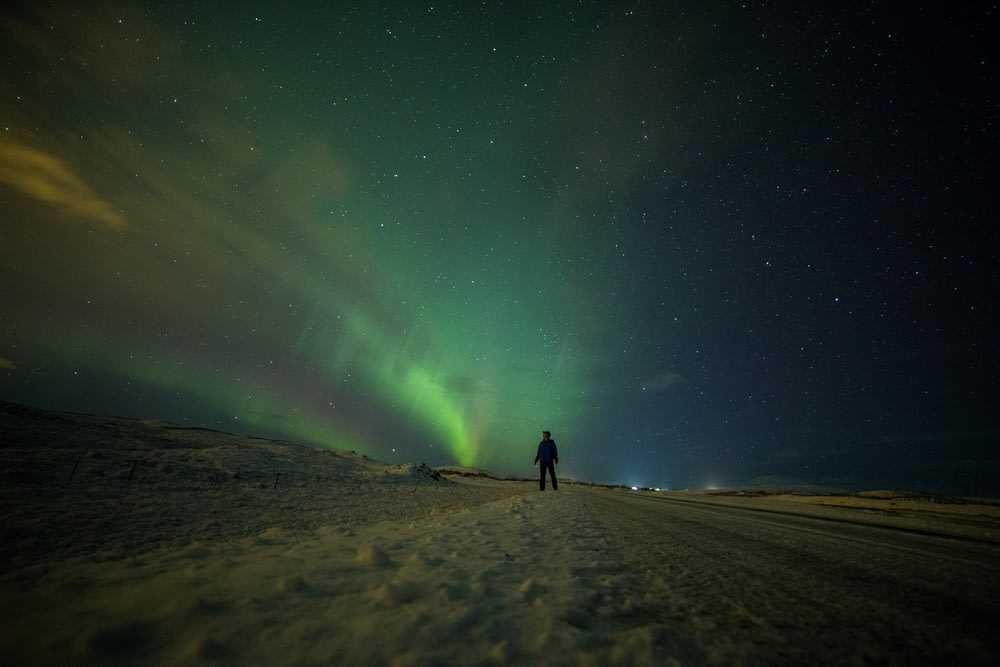 silhouette of person standing on brown sand under northern lights
