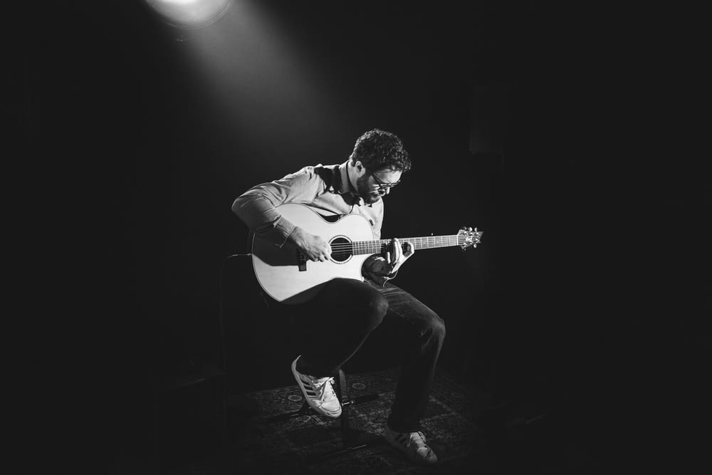 Photo en niveaux de gris d’un homme jouant de la guitare sur scène