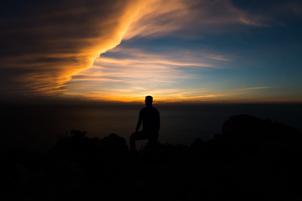 silhouette of person sitting on rock formation at golden hour