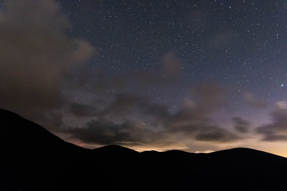 silhouette of mountain under starry sky at sunset